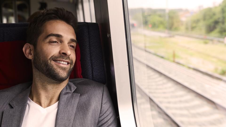 A man in a blazer on a train smiling and looking out of the window